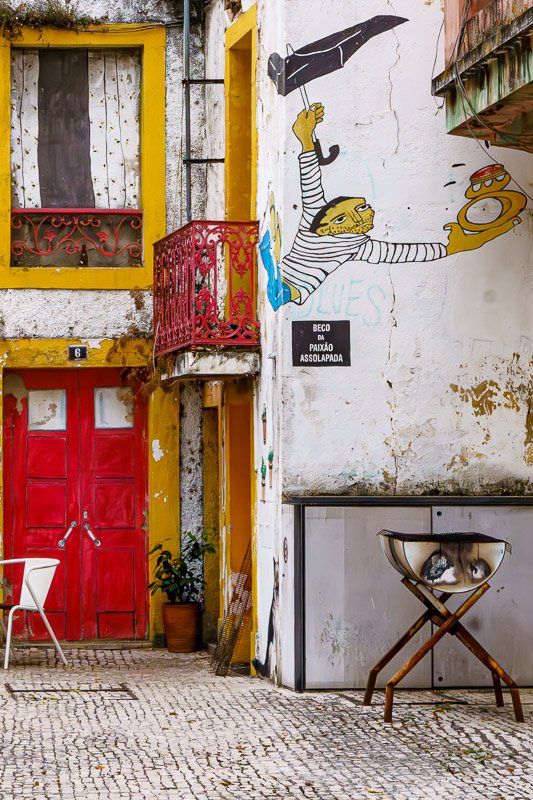 Could not look away_7 Peeling yellow wall with painted figures and a vivid red door, urban texture, Portugal