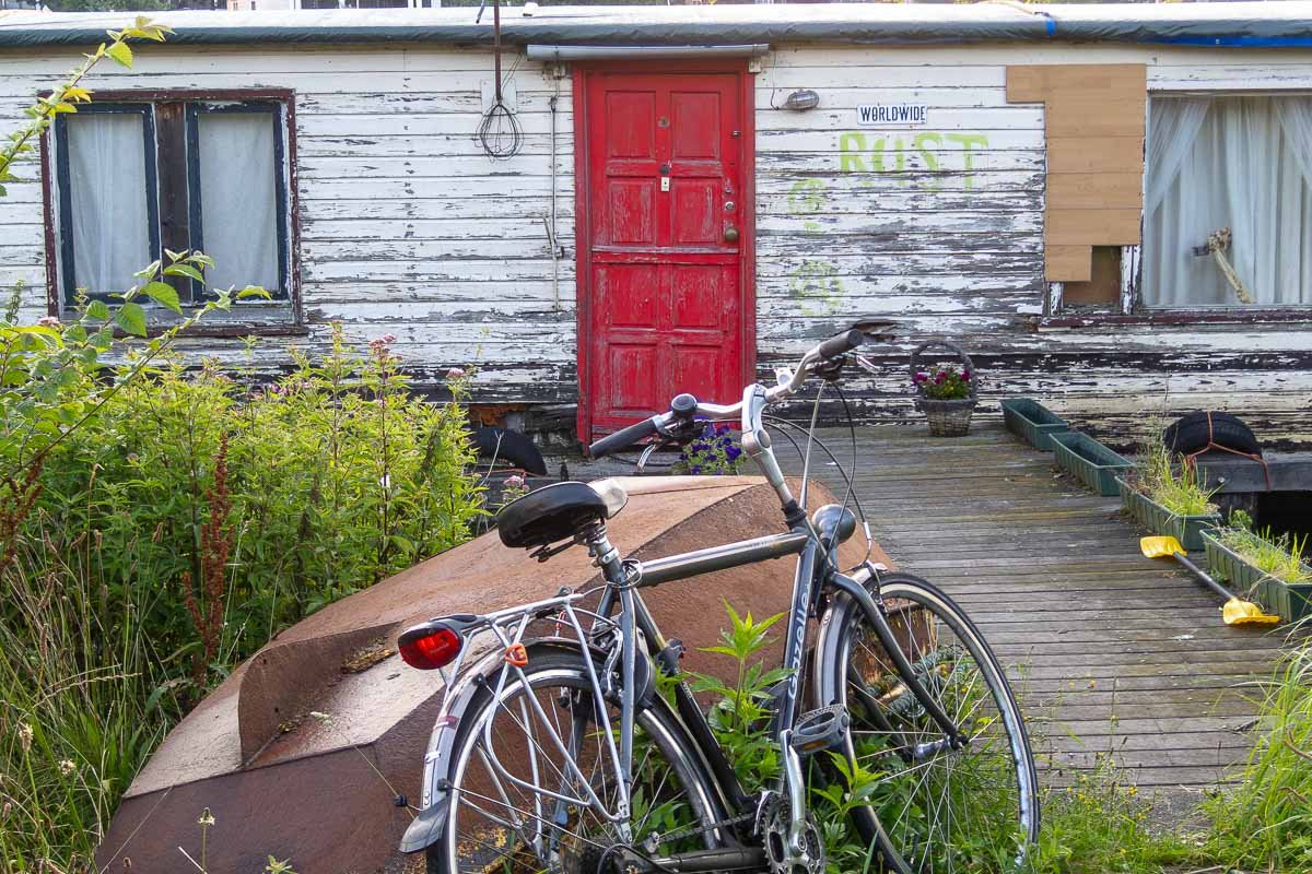 Europe H_11 Weathered white houseboat with red door and RUST graffiti, bicycles in foreground, Amsterdam canal