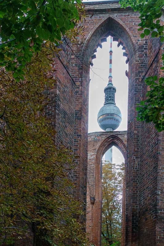 Europe H_13 Berliner Fernsehturm framed through the gothic arched ruin of Anhalter Bahnhof, Berlin, overgrown brick walls and ivy
