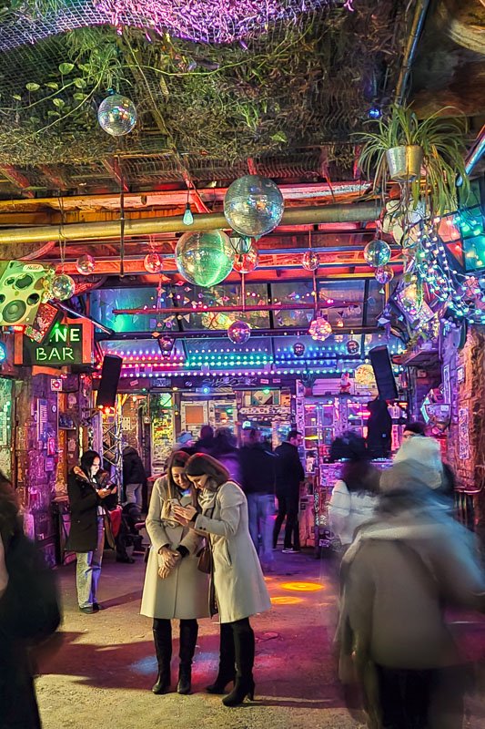 Europe H_2 Crowded interior of Szimpla Kert ruin bar in Budapest, disco balls and neon lights overhead, figures in motion