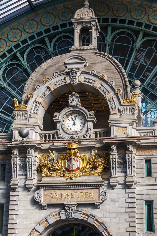 Europe H_5 Clock and gilded coat of arms on the facade of Antwerp Centraal railway station, ornate stone arch and iron canopy