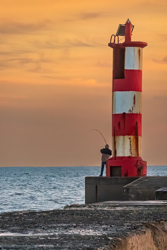 Found_9 Red and white striped lighthouse at dusk with a lone figure standing at its base, Atlantic behind
