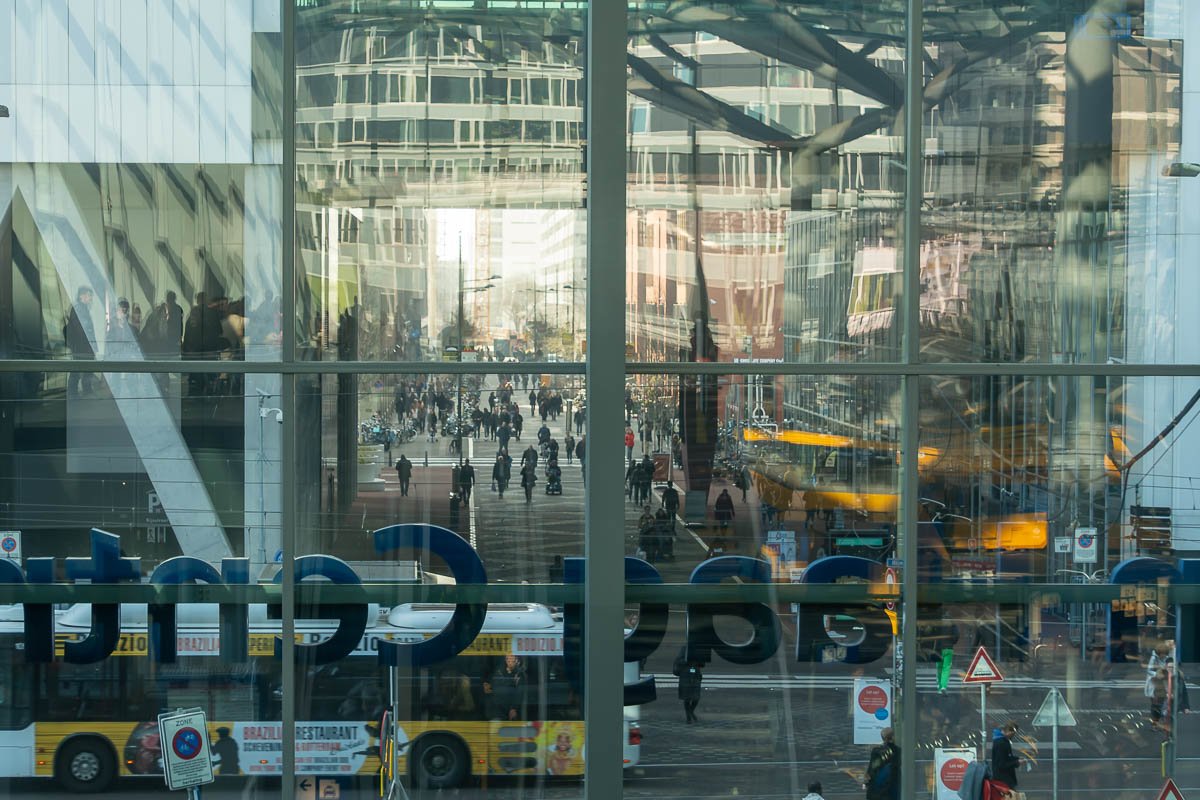 Movement Modern glass transit hub with layered reflections, buses visible through the lower level