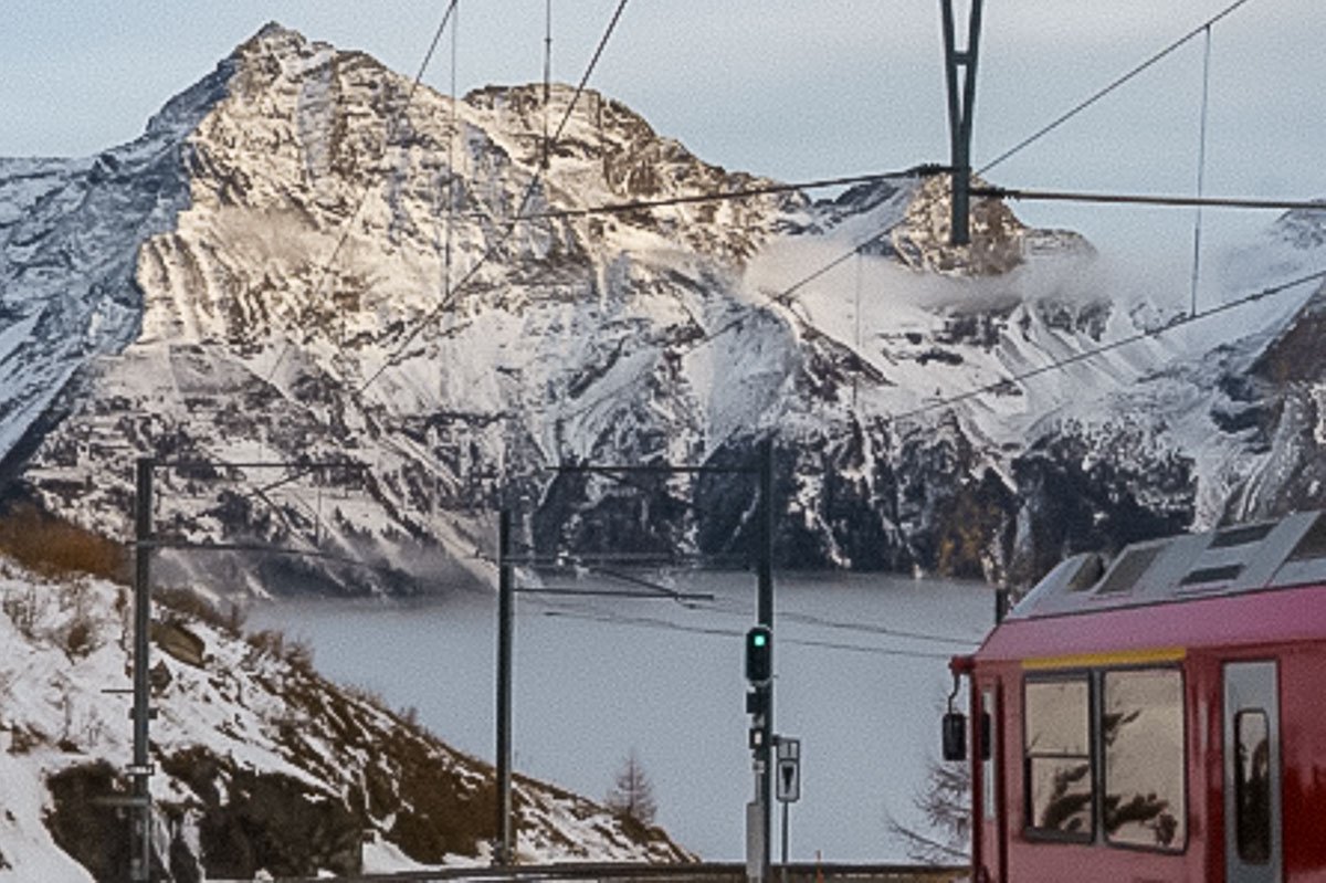 Movement_5 Red mountain train on a narrow track, deep snow and sharp peaks rising behind