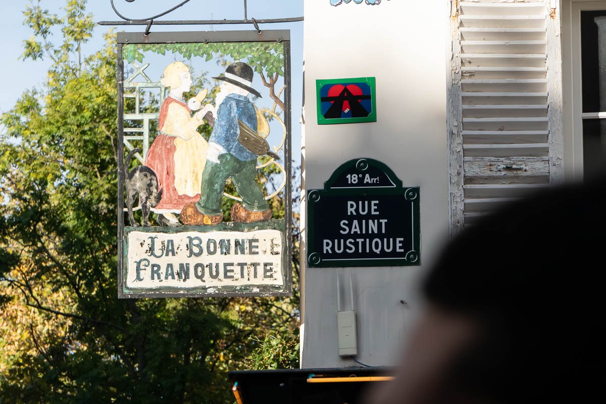Signs_1 Vintage painted inn sign reading La Bonne Franquette beside a green Paris street plate for Rue Saint Rustique, 18th arrondissement