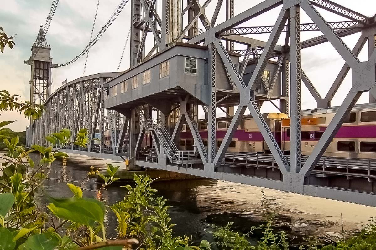 US_Housesit_17 Steel truss lift bridge over the Cape Cod Canal at sunset, commuter rail train passing through, golden light on water