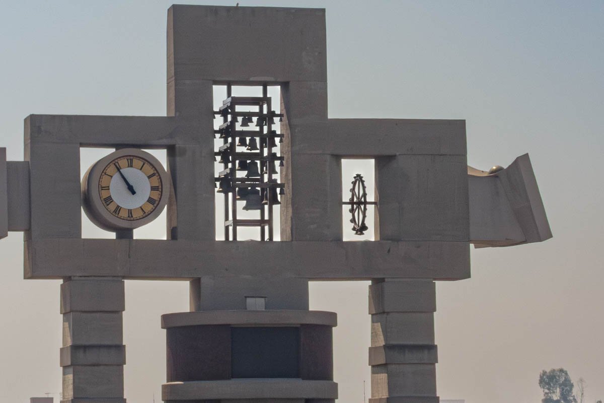 clocks_2 Abstract concrete clock sculpture in a brutalist cross-shaped form against a grey sky
