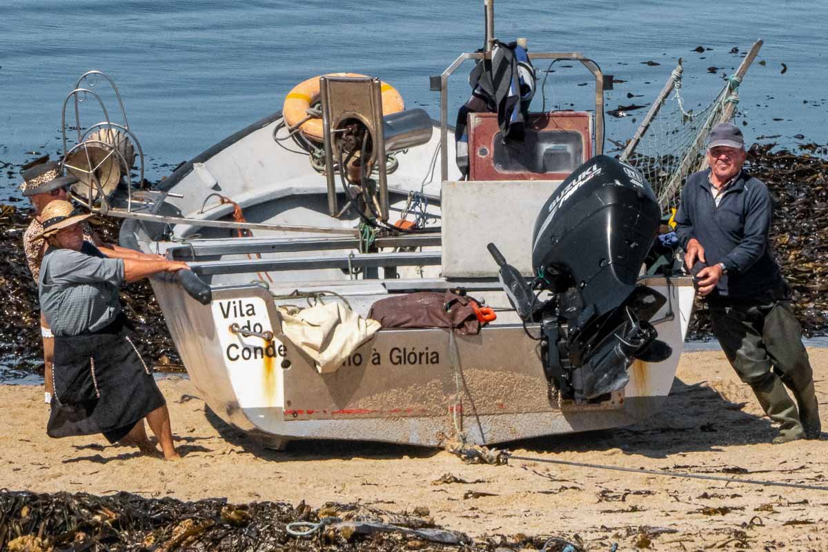 download Fishing boat lettered Vila do Conde with two women and a man pushing it onto sand, Vila Cha