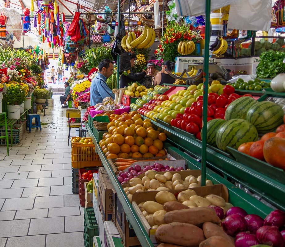markets_10 Long narrow aisle between overflowing produce stalls, receding perspective, shoppers in distance