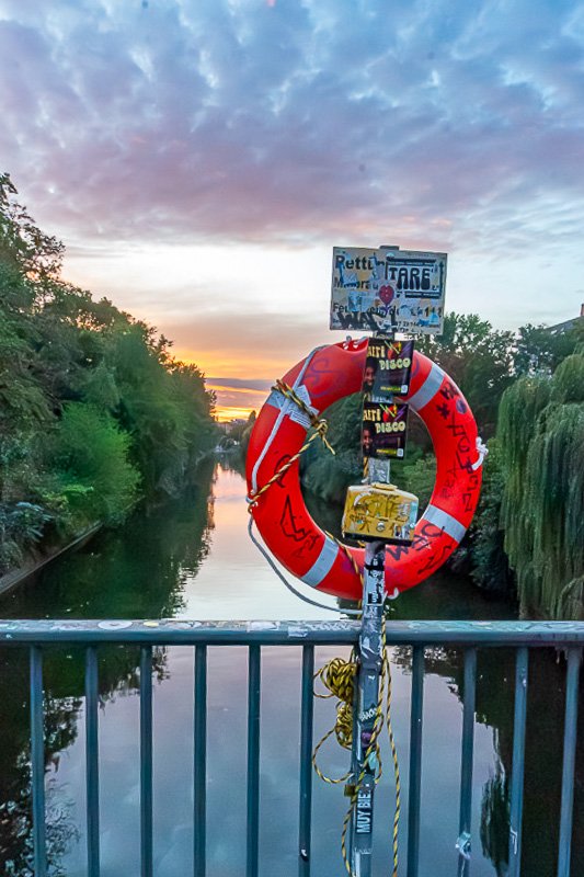 signs_9 Red and white life preserver mounted on a bridge railing above a calm river at dusk