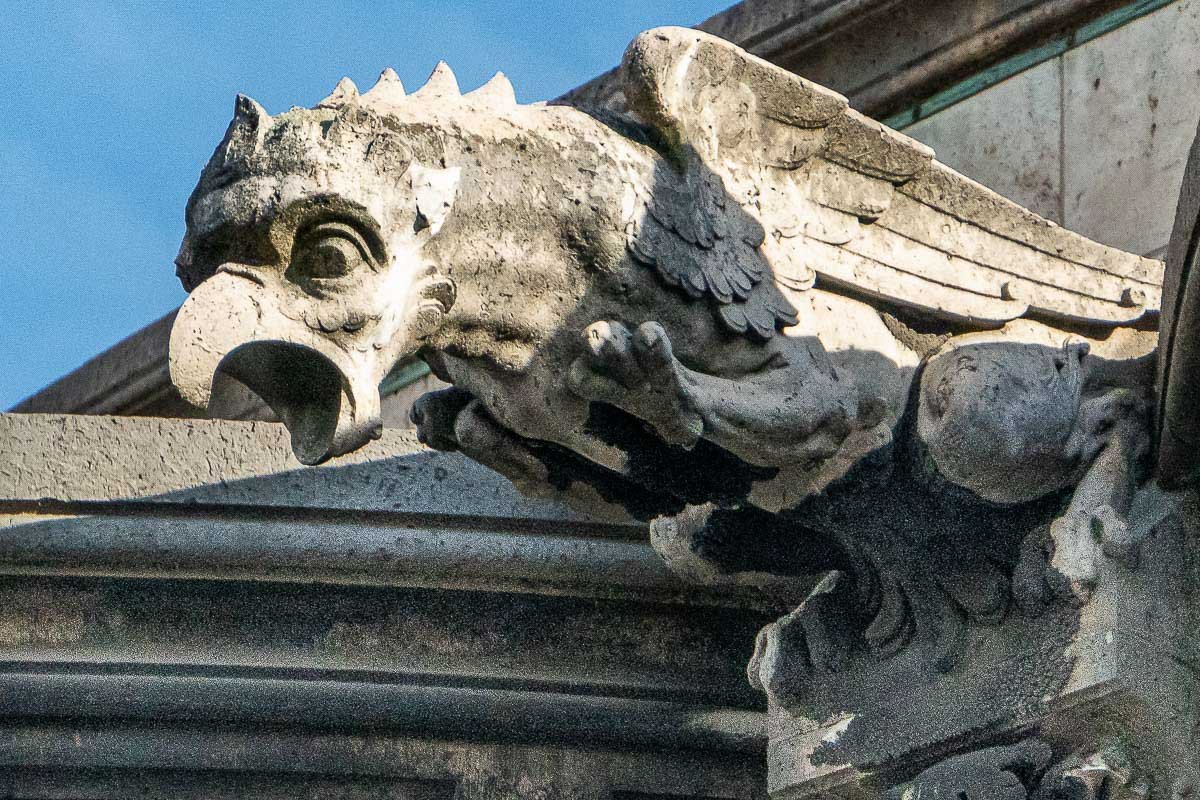 watchers_3 Close view of a dark stone gargoyle with skull-like features, carved architectural detail