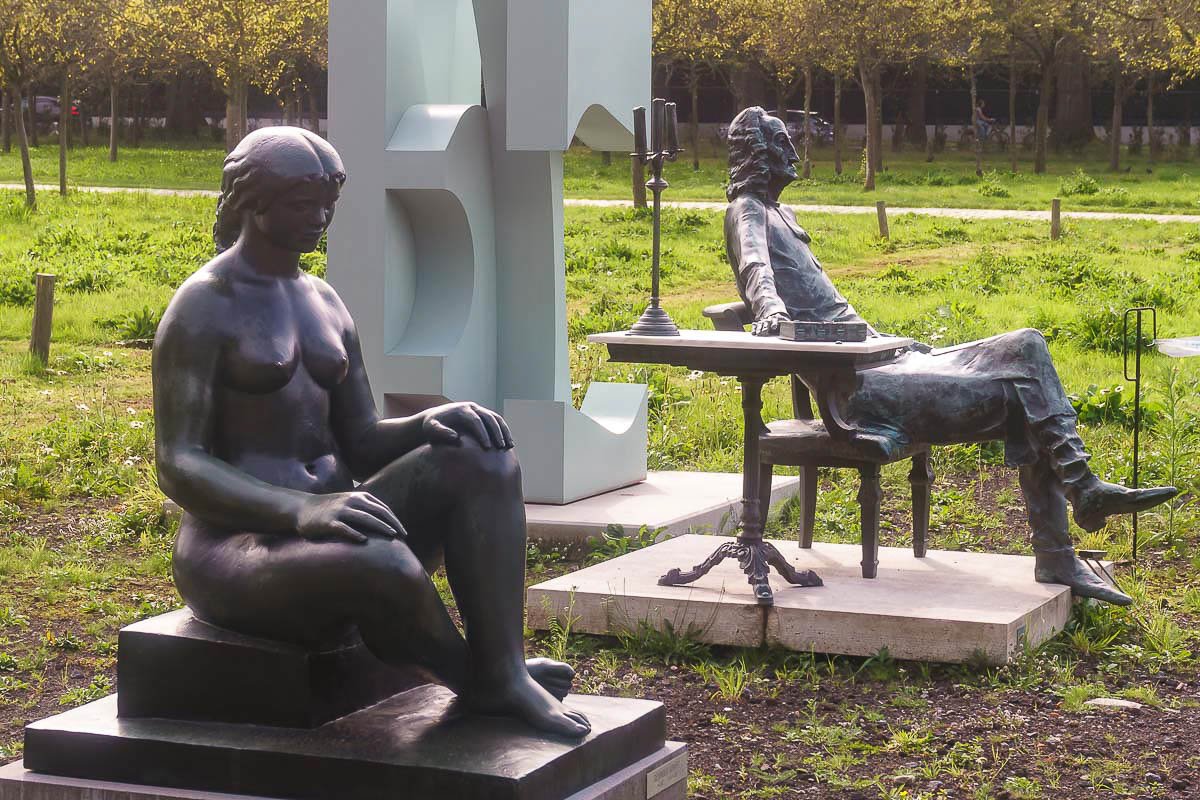 watchers_4 Two small bronze figures seated at a table in an open landscape, contemplative and still