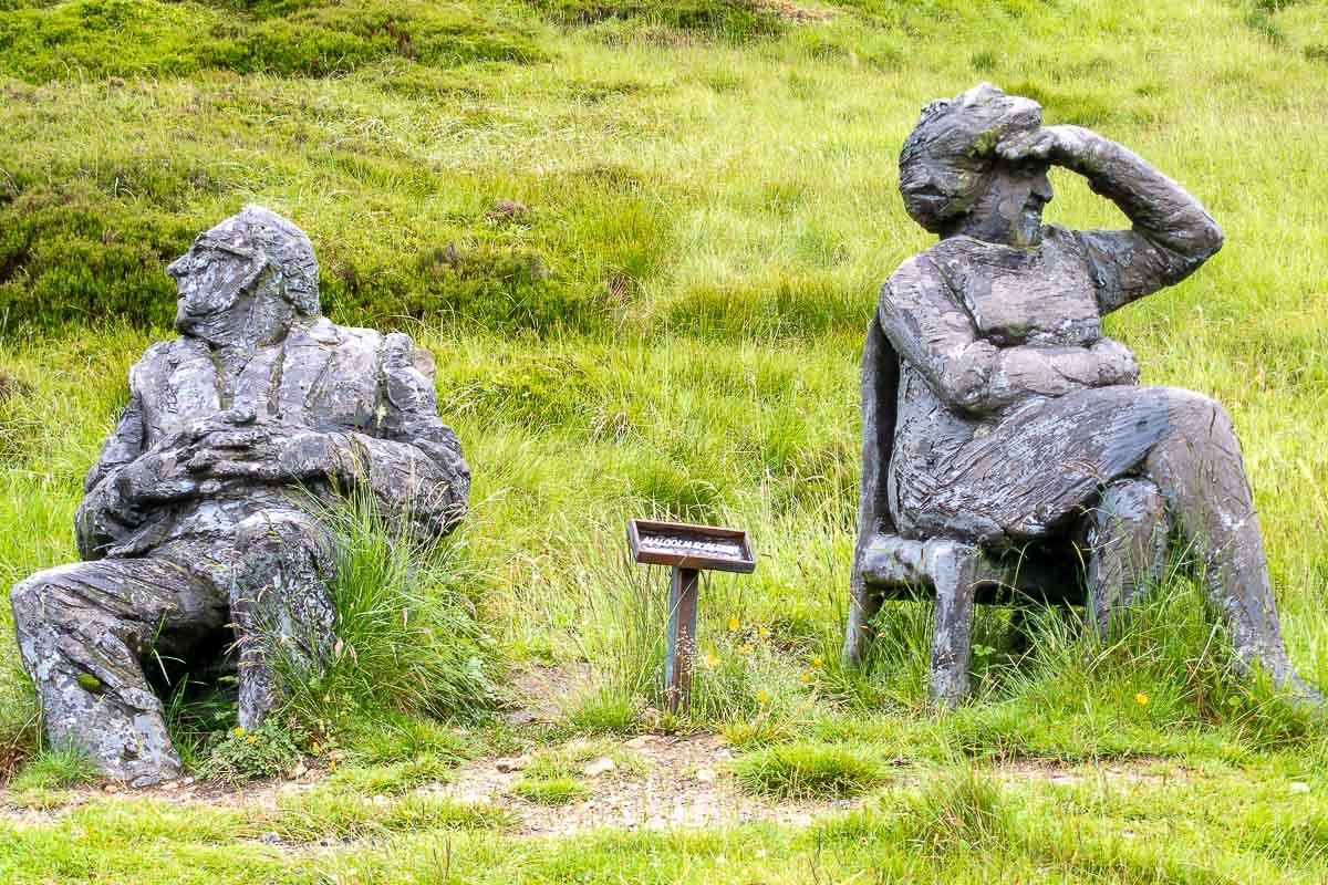 watchers_7 Weathered stone figure of a seated reader on a hillside bench, relaxed, almost human